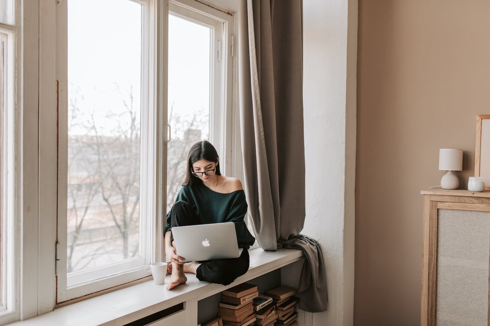 remote job search strategies - Young female freelancer sitting with laptop on windowsill at home