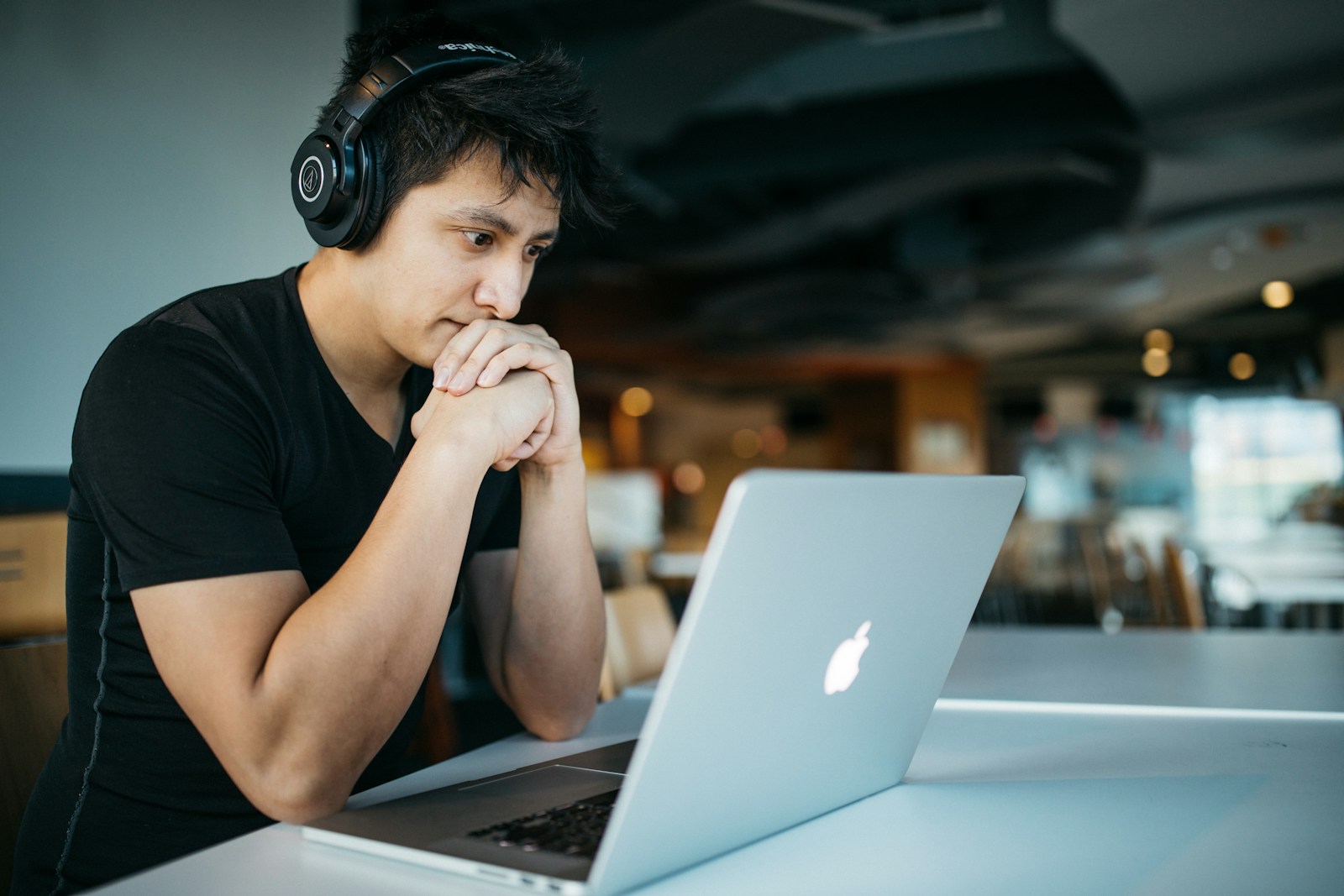 teach english online -man wearing headphones while sitting on chair in front of MacBook